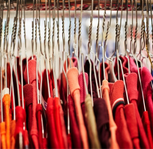 Portant de vêtements : rangée de cintres en métal tenant des habits rouges et colorés.