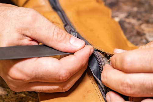 artisant en train de découdre un zip sur un sac en cuir